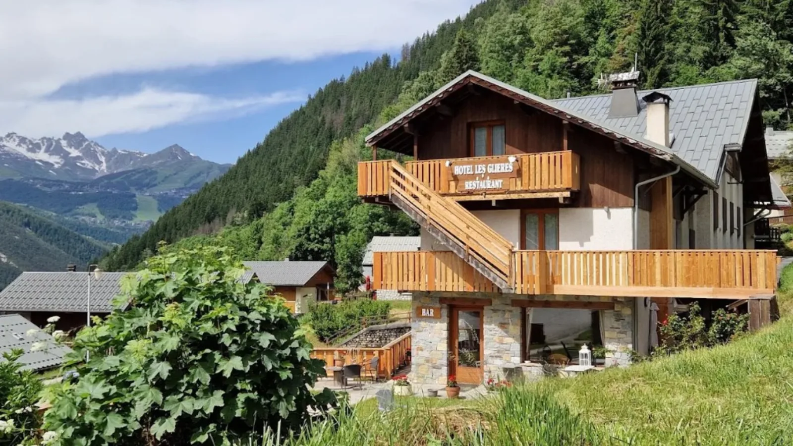 Hôtel Les Glières in summer: wooden balconies, restaurant terrace and snow-capped peaks behind Champagny-en-Vanoise